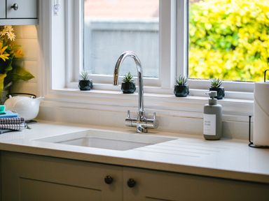 A kitchen sink with a chrome faucet and small potted plants on the windowsill at Polished Pebble in Beadnell