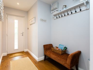An entryway with a white door a brown bench with a basket and a wall-mounted shelf with hooks at Polished Pebble in Beadnell