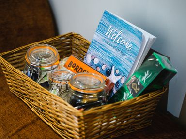 A wicker basket with three glass jars a welcome visitor guest book and packaged snacks at Polished Pebble in Beadnell
