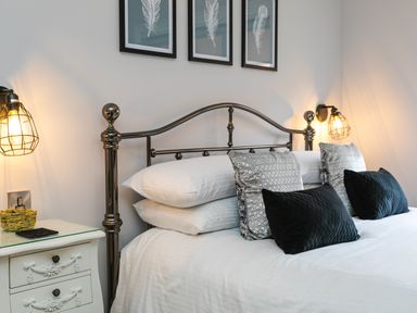 A bedroom with a metal bed frame white bedding pillows nightstand and wall lamps at Polished Pebble in Beadnell