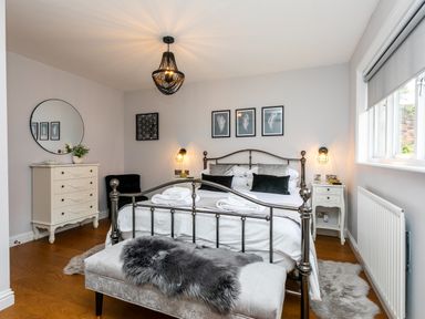 A bedroom with a metal bed frame bedside tables a chest of drawers a round mirror and a window at Polished Pebble in Beadnell