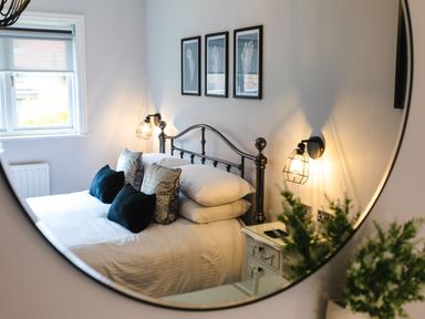 A bedroom with a metal bed frame cushions on the bed bedside table with a lamp and framed artwork above the bed at Polished Pebble in Beadnell