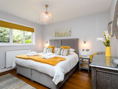 A bedroom with a bed with yellow and gray pillows a window with a yellow blind and a bedside table with a lamp at Polished Pebble in Beadnell