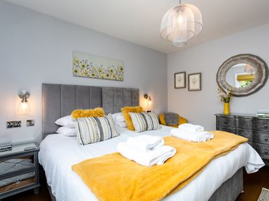 A bedroom with a double bed yellow blankets and pillows a mirrored dresser and wall art at Polished Pebble in Beadnell