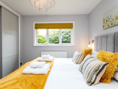 A bedroom with a bed with yellow pillows and blanket white towels on the bed a window with a yellow blind and a built in wardrobe at Polished Pebble in Beadnell