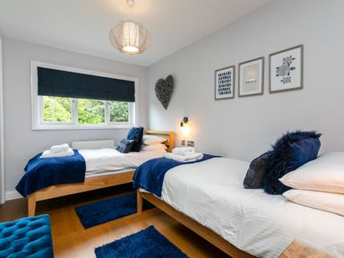 A bedroom with two single beds blue rugs and cushions and framed pictures on the wall at Polished Pebble in Beadnell