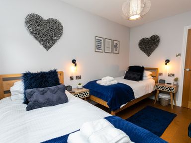 A bedroom with two single beds blue throws and pillows heart wall decorations at Polished Pebble in Beadnell
