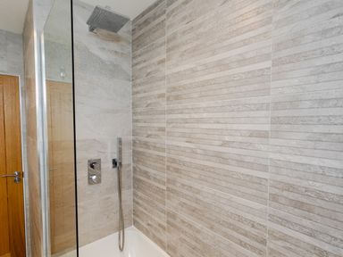 A shower area with a glass panel a wall-mounted showerhead and tiled walls at Polished Pebble in Beadnell