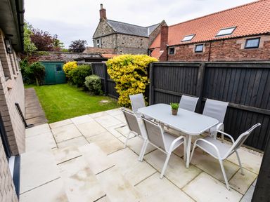A backyard patio with a rectangular table and six chairs next to a lawn and garden shed at Polished Pebble in Beadnell