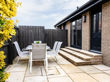 An outdoor patio with a table and six chairs next to brick steps and black doors at Polished Pebble in Beadnell