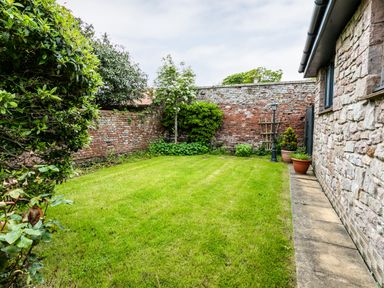 A garden with a lawn next to a stone house and a brick wall at Polished Pebble in Beadnell