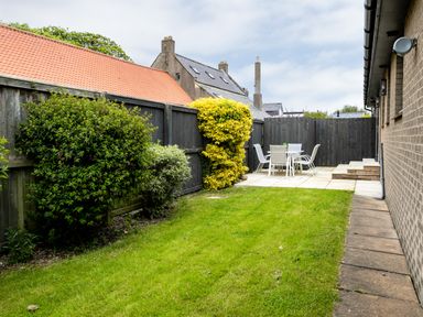 A backyard with a lawn a paved patio area with a table and chairs and wooden fencing at Polished Pebble in Beadnell