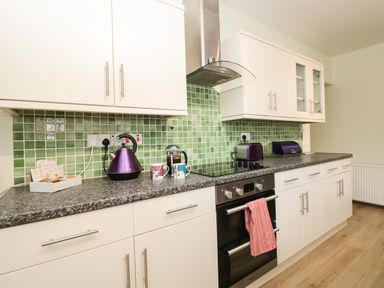 A kitchen with white cabinets green tile backsplash and various appliances at Creel Cottage Blackwood Street in Amble