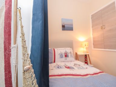 A bedroom with a single bed dressed in patterned bedding a bedside table with a lamp and wall art at Creel Cottage Blackwood Street in Amble