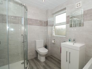 A bathroom with a glass shower, toilet, sink, mirror, and window at Creel Cottage Blackwood Street Amble