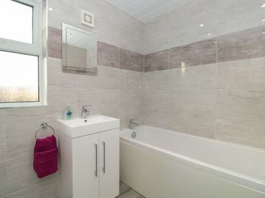 A bathroom with a bathtub a sink with cabinet mirror and a window at Creel Cottage Blackwood Street in Amble