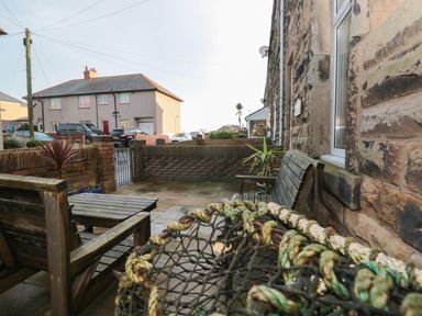 A stone patio with wooden benches and table surrounded by brick walls at Creel Cottage Blackwood Street in Amble