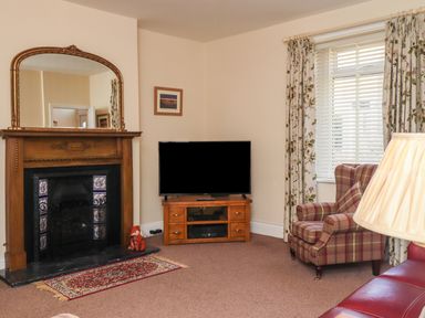 A living room with a fireplace mirror and television beside a plaid armchair at Creel Cottage Blackwood Street in Amble