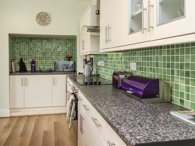 A kitchen with green tiled backsplash white cabinets and black countertop at Creel Cottage Blackwood Street in Amble