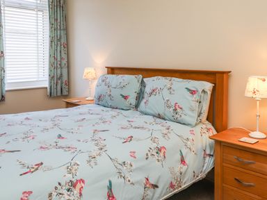 A bedroom with a wooden bed frame bird patterned bedding blue curtains bedside tables and lamps at Creel Cottage Blackwood Street in Amble