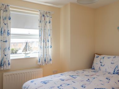 A bedroom with a bed near a window with curtains and a decorative sailboat at Creel Cottage Blackwood Street in Amble