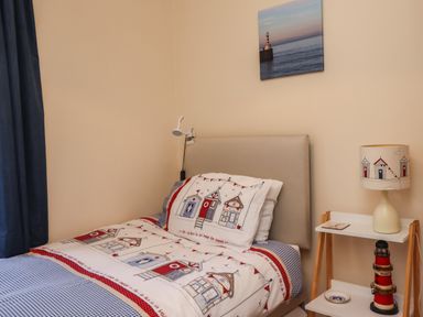 A bedroom with a single bed and a nightstand with a lamp and lighthouse model at Creel Cottage Blackwood Street in Amble