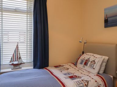 A bedroom with a single bed near a window with blinds and dark curtains a small model sailboat on the windowsill and a lighthouse photo on the wall at Creel Cottage Blackwood Street Amble