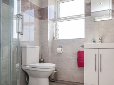 A bathroom with a toilet a white vanity unit a pink towel and a window at Creel Cottage Blackwood Street in Amble