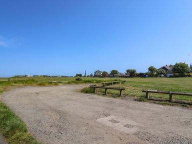 A gravel road with wooden barriers and grassy fields with houses in the distance at Creel Cottage Blackwood Street in Amble