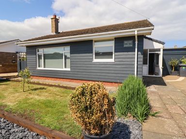 A single-story house with blue siding and white trim with a front garden and walkway at Willow in Beadnell