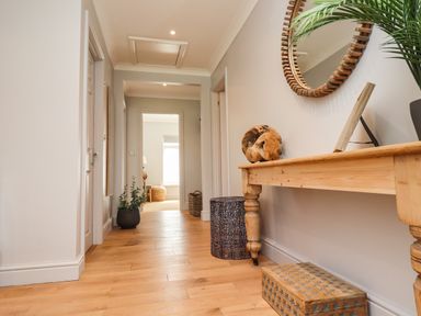 A hallway with wooden floor a table mirror plant and basket at Willow Beadnell
