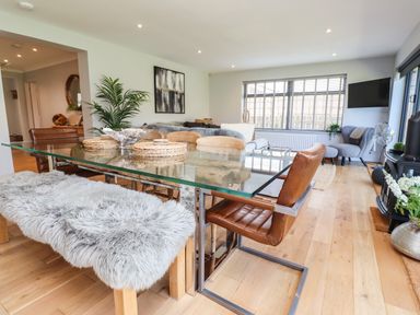 A dining area with glass table and chairs with a living room area with armchairs and a TV at Willow in Beadnell