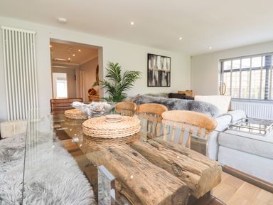 A dining area with a glass top wooden table surrounded by chairs next to a living room with a sofa and window blinds at Willow in Beadnell
