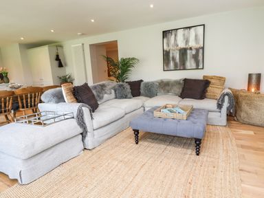 A living room with a large sectional sofa a gray ottoman and a woven rug at Willow in Beadnell