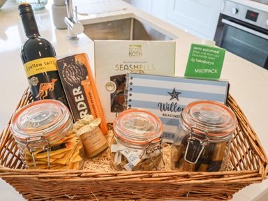 A wicker basket with jars of tea and snacks a bottle of wine and a carton of milk on a kitchen counter at Willow Beadnell
