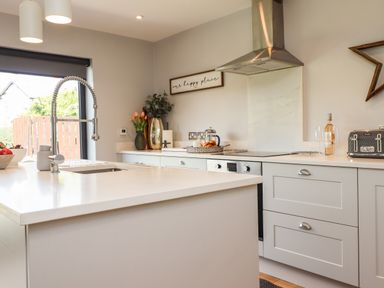 A kitchen with a sink faucet on an island and counter spaces with a toaster and a bottle at Willow in Beadnell