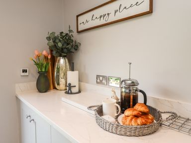 A kitchen countertop with a tray holding croissants coffee a mug and a French press next to vases with flowers and a paper towel holder at Willow in Beadnell