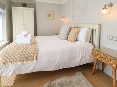 A bedroom with a white bed and cushions a wooden wardrobe and bedside table at Willow in Beadnell
