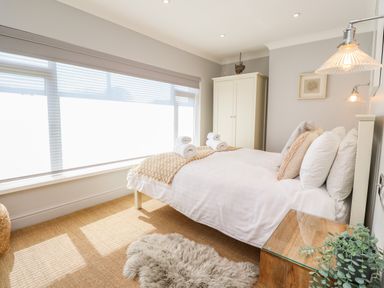 A bedroom with a bed with white linens and rolled towels next to a window with blinds at Willow in Beadnell