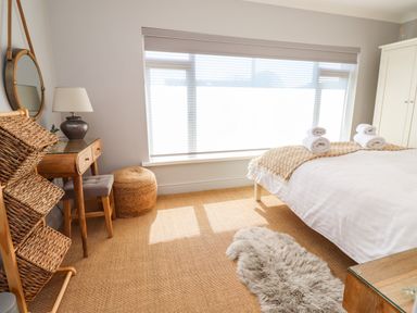 A bedroom with a bed with rolled towels a wicker basket a dressing table with a mirror and lamp and a wardrobe at Willow in Beadnell