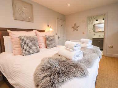 A bedroom with a bed with pillows and folded towels with a door leading to a bathroom at Willow in Beadnell