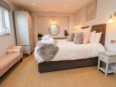 A bedroom with a bed with pillows and folded towels a bench a wardrobe a round mirror and bedside tables at Willow in Beadnell