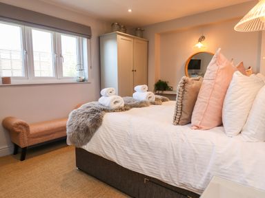 A bedroom with a bed with pillows and rolled towels a bench a wardrobe and a round mirror at Willow in Beadnell