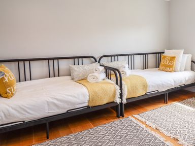 A bedroom with two single beds with black metal frames yellow throws and pillows and rolled white towels on wooden floor at Willow in Beadnell
