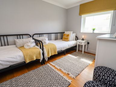 A bedroom with two single beds a side table with a lamp window and patterned rugs at Willow in Beadnell