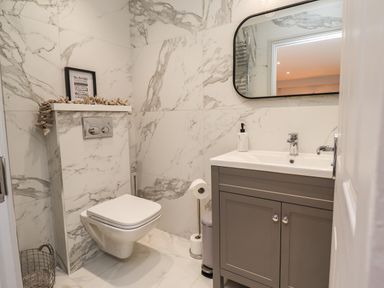A bathroom with a wall mounted toilet and a vanity unit with a sink and mirror at Willow in Beadnell