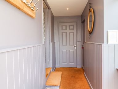 A hallway with gray paneled walls a closed gray door a wooden coat rack and a round mirror with hooks at Willow in Beadnell