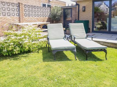 Two lounge chairs on grass near a patio and flower bush at Willow in Beadnell