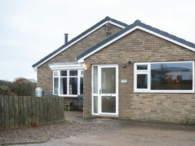 Front view of a brick bungalow with white framed windows and door a wooden fence and gravel driveway at Our Story Cottage in Longhoughton