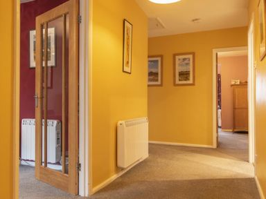 A hallway with yellow walls, carpeted floor, framed pictures on walls, and a wooden door with glass panels at Our Story Cottage Longhoughton